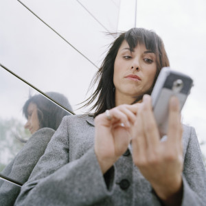 Business woman standing outside in front of office building, using mobile phone